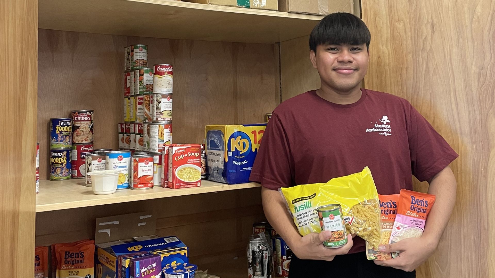 A student stands in the Food Pantry holding non-perishible food items