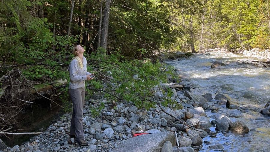 An intern stands in a rocky riverside spot operating a drone