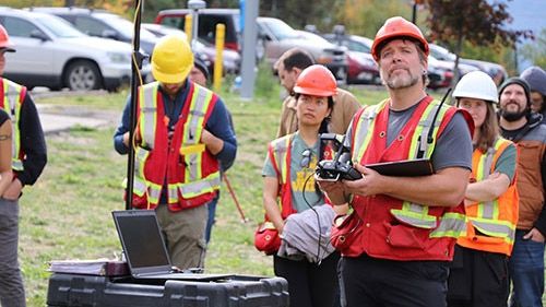 Students and an instructor wearing orange vests fly drones