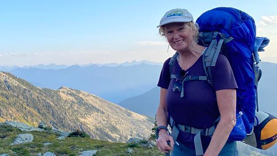 Allison Alder stands in the alps wearing a hiking backpack